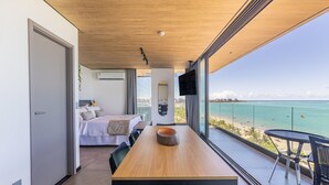 A modern bedroom with a bed, bedside table, and a large window overlooking a beach. - NWTs - Apartamentos com Vista Frente-Mar (Maceió)