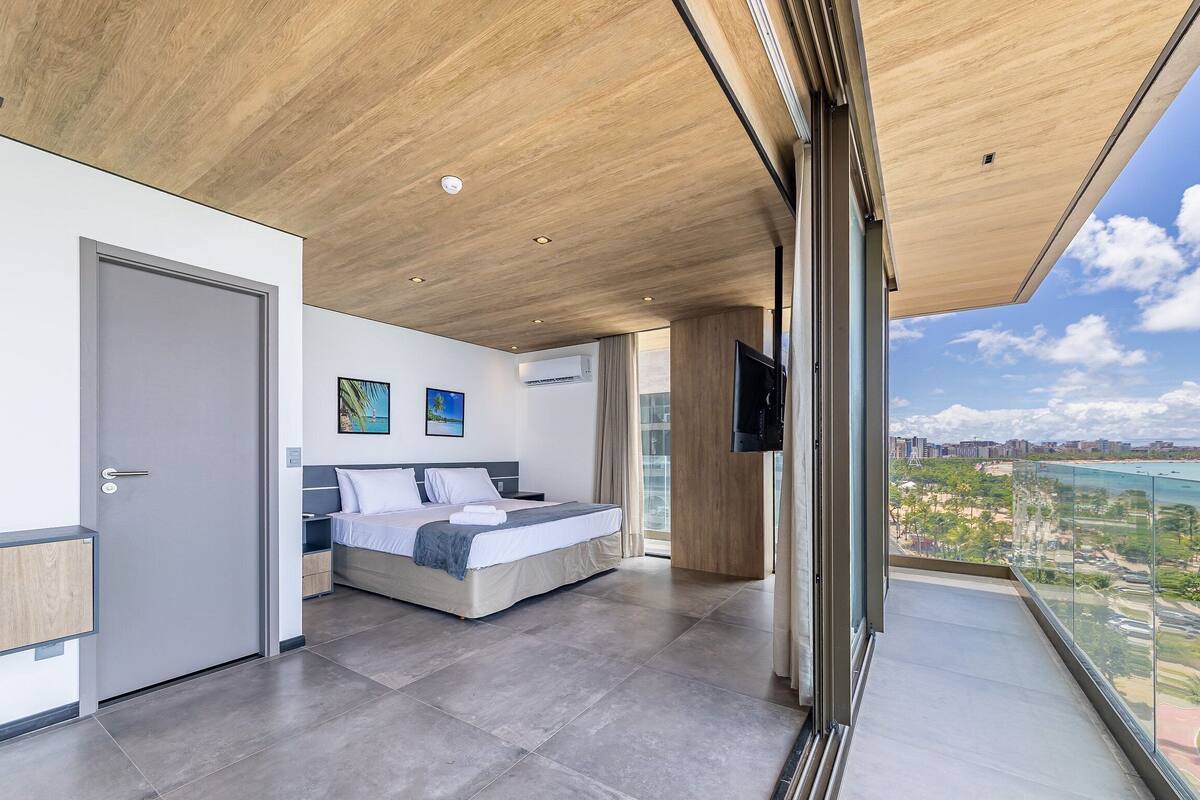A modern hotel room with a large bed, a TV, and a balcony with a city view.