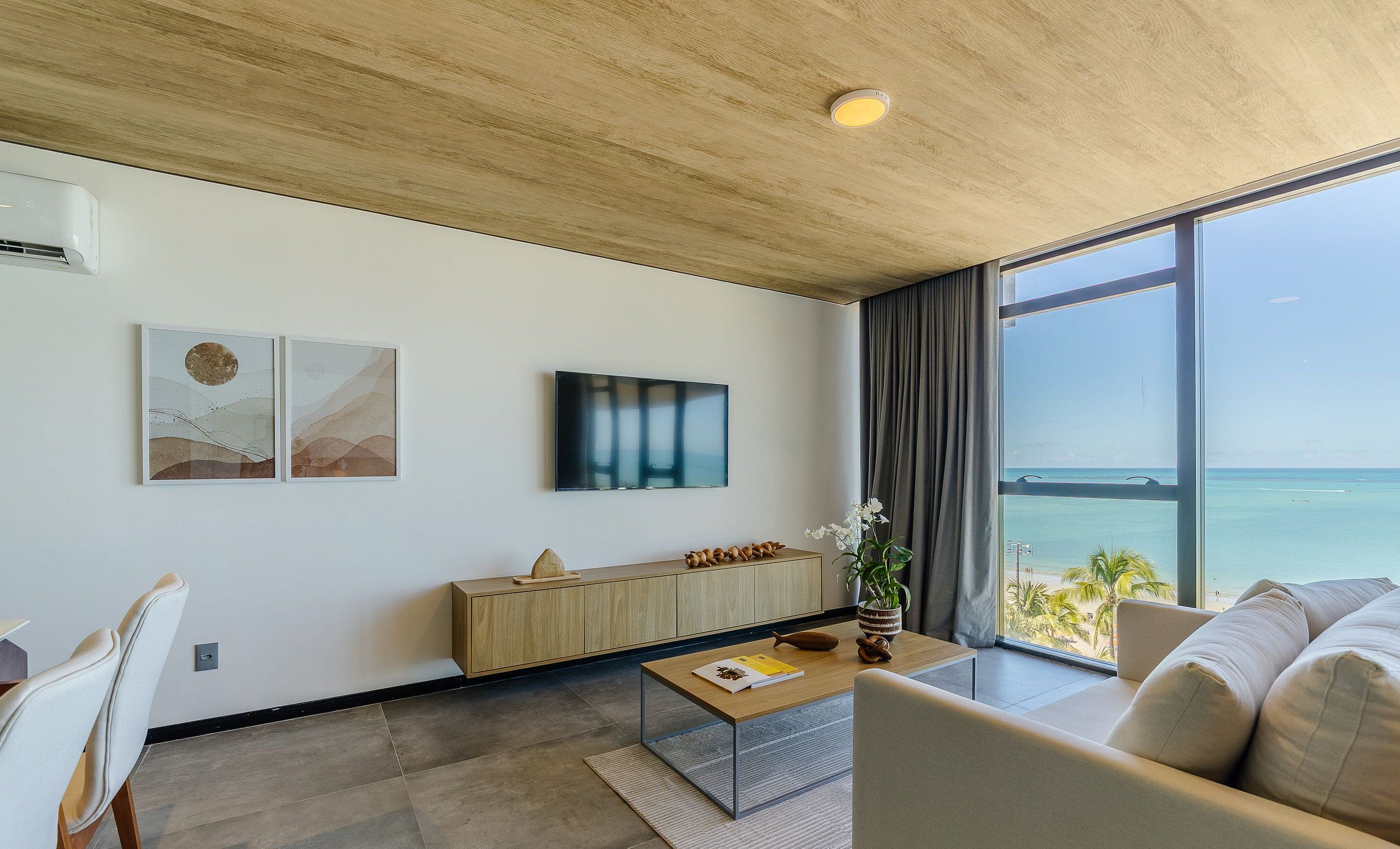 A modern living room with a large window offering a view of the sea, a wooden ceiling, and a minimalist design.