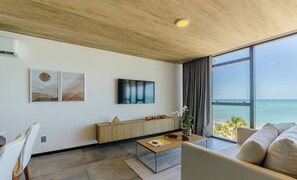 Un salon moderne doté d’une grande fenêtre donnant sur la mer, d’un plafond en bois et d’un aménagement minimaliste.