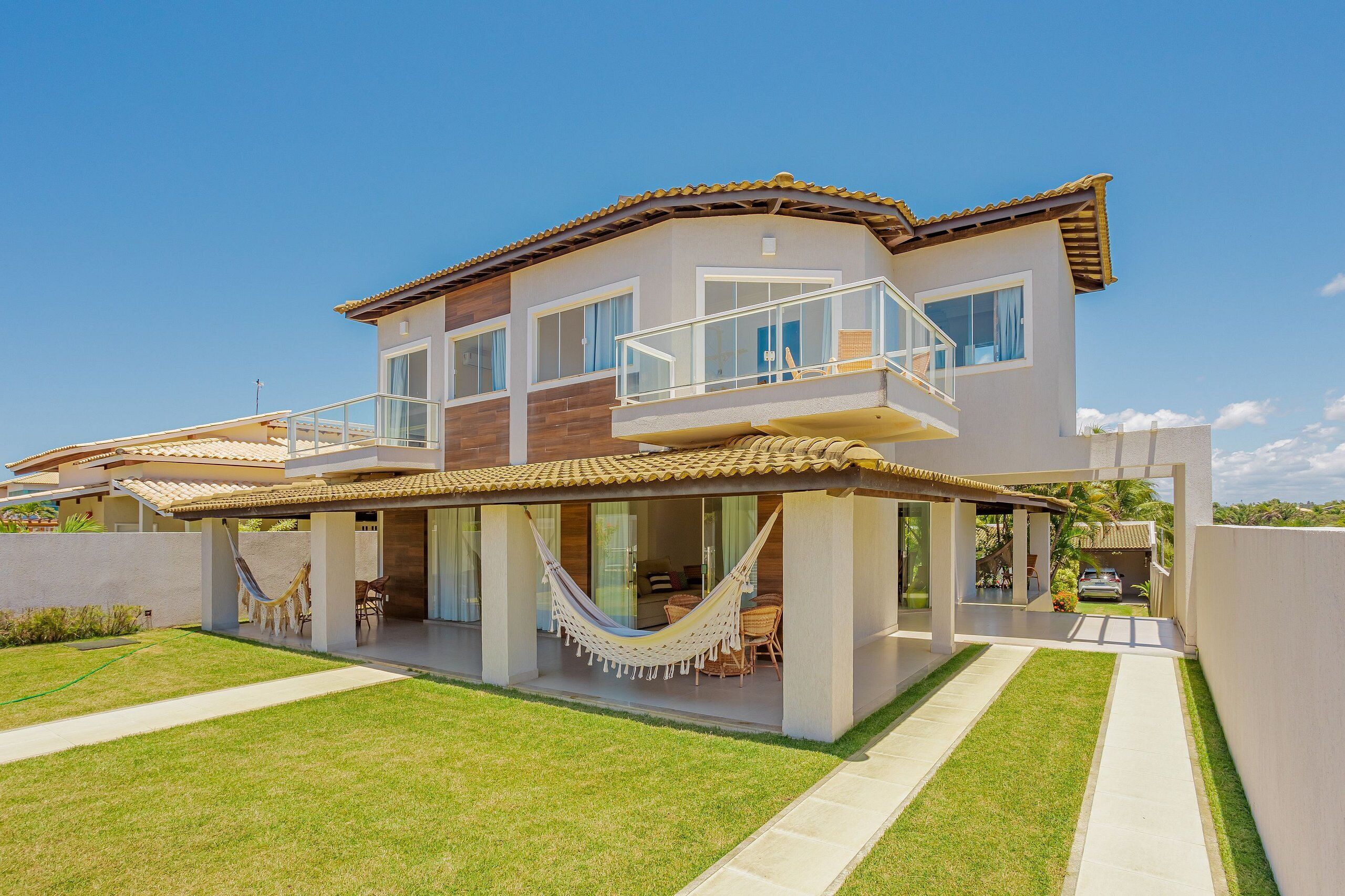 Une maison moderne à deux étages, dotée d’un balcon, d’un hamac et d’une pelouse bien entretenue.