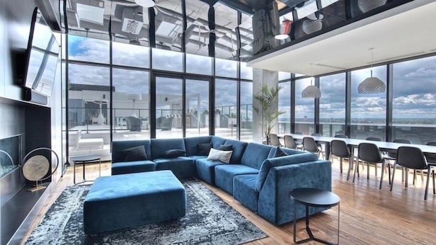 A modern living room with a blue sectional sofa, a small round table, and a large window offering a city view.