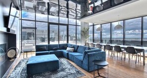 Een moderne woonkamer met een blauwe modulaire bank, een kleine ronde tafel en een groot raam met uitzicht op de stad.