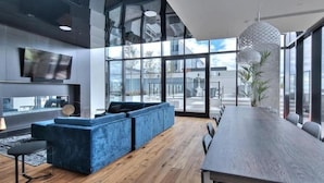 A modern interior with a large wooden table, blue sofas, and large windows offering views of the city.