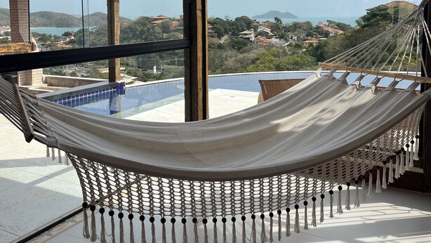 A hammock on a balcony with a view of a swimming pool and distant buildings.