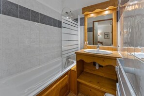 A bathroom with a bathtub, a wooden vanity with a sink, and a mirror. - Resort center, 3rd floor, fitness, swimming pool, sauna, balcony, tv, ski locker, 33m², Les Orres (Les Orres)