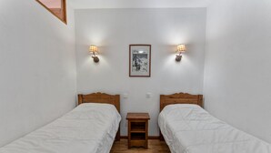 A small, clean room with two single beds, a nightstand, and two wall-mounted lamps.