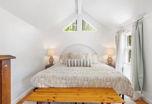 A bedroom with a bed, bedside lamps, a wooden bench, and a window with curtains.