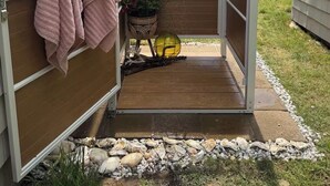 Asoleadero de madera con ducha tipo lluvia, un perchero y una planta en maceta.