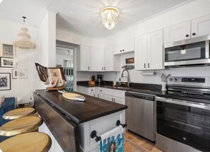 A kitchen with white cabinets, a central island with stools, a chandelier, and modern appliances including a dishwasher and oven. - Charming 3-bedroom cottage with AC and WiFi in Wells: Welcome to the SheShell (wells)