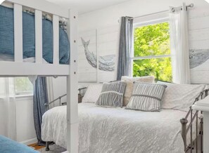 A bedroom with a bunk bed, a window with curtains, and wall art. - Charming 3-bedroom cottage with AC and WiFi in Wells: Welcome to the SheShell (wells)