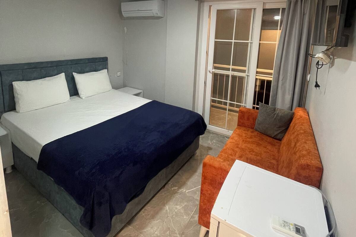 Ein Hotelzimmer mit einem Bett, einem Sofa, einem kleinen Tisch, einer Klimaanlage, einem Fernseher und einer Glastür zum Balkon.