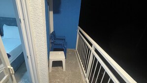 Un balcon étroit avec une balustrade blanche, un petit tabouret et une chaise bleue.