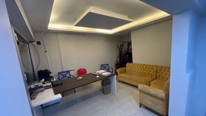 Un salon moderne avec un canapé, une table basse et un téléviseur. On y trouve également des chaises et un ballon rouge pour faire de l’exercice. Le sol est carrelé et le plafond est doté d’un éclairage encastré.