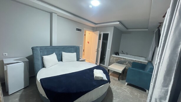 Une chambre d’hôtel moderne avec un lit rond, une petite table de chevet, une banquette intégrée, une salle de bain avec baignoire et un grand miroir.