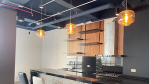 Eine moderne Küche mit schwarzem Arbeitsplatz, Edelstahlgeräten und Holzschränken. Drei Pendelleuchten hängen über der Arbeitsfläche.