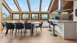 Une cuisine moderne dotée d’un grand îlot central, de poutres en bois et de grandes fenêtres.