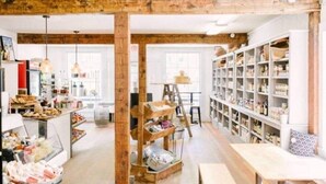 A spacious room with wooden beams, a central wooden structure, and a long shelf unit filled with jars and containers.
