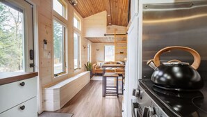 A modern kitchen with a large stove and kettle, wooden beams on the ceiling, and large windows offering a view of the outdoors. - Sage House Glamping Retreat with Hot Tub + Sauna (Chester)