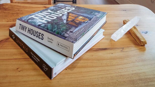 A wooden interior with a book titled "Tiny Houses" on a table, a ceiling fan, and a kitchen area in the background. - Sage House Glamping Retreat with Hot Tub + Sauna (Chester)