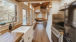 A compact kitchen with wooden cabinets, a stainless steel refrigerator, and a built-in oven. - Sage House Glamping Retreat with Hot Tub + Sauna (Chester)