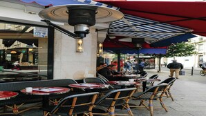 Outdoor seating with tables and chairs, a covered area with a striped awning, and a street view with pedestrians.