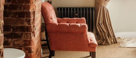 A room with a brick fireplace, a red armchair, a painting on the wall, and a window with curtains.