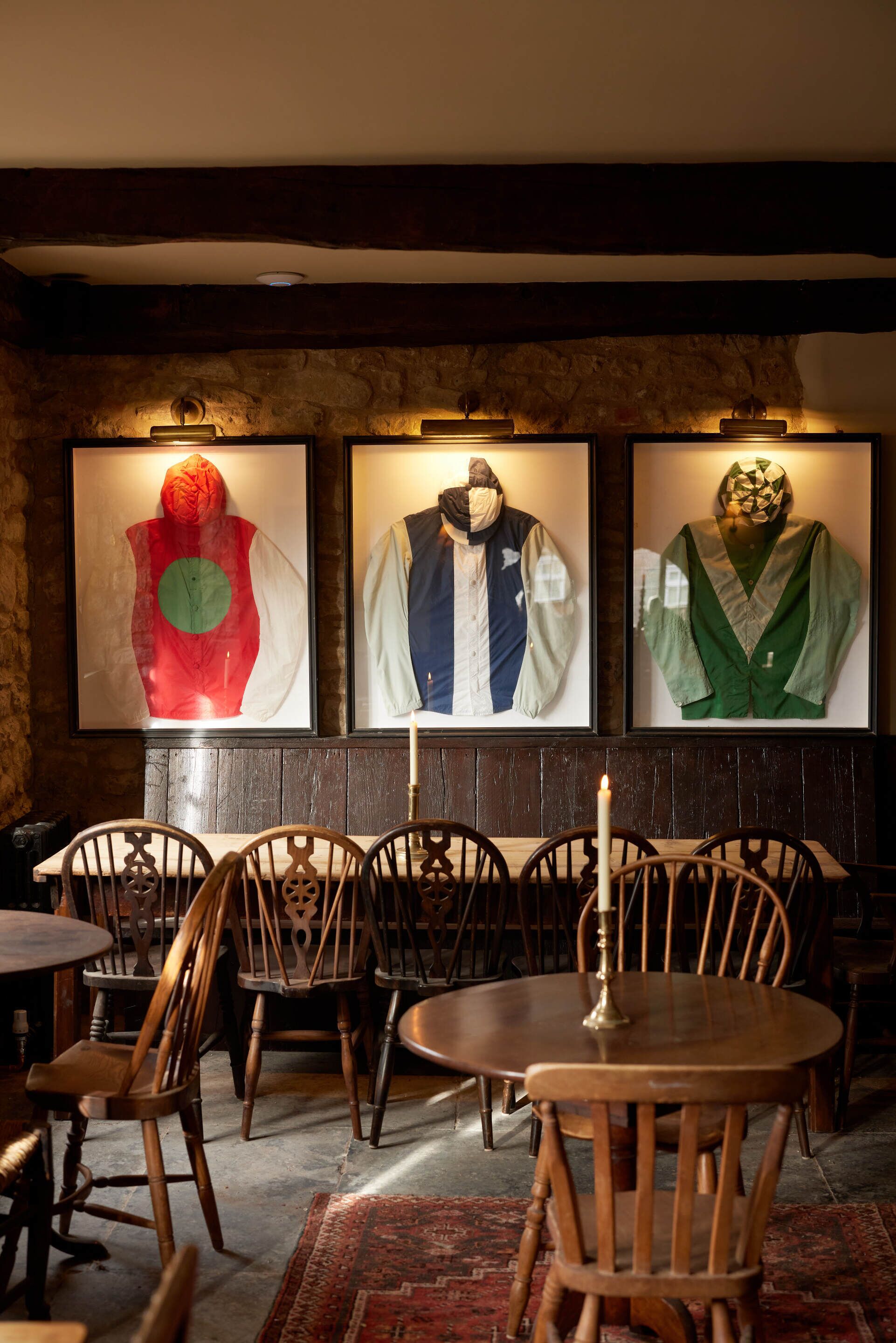 A restaurant interior with wooden chairs and tables, a stone wall, and framed artwork on the wall.