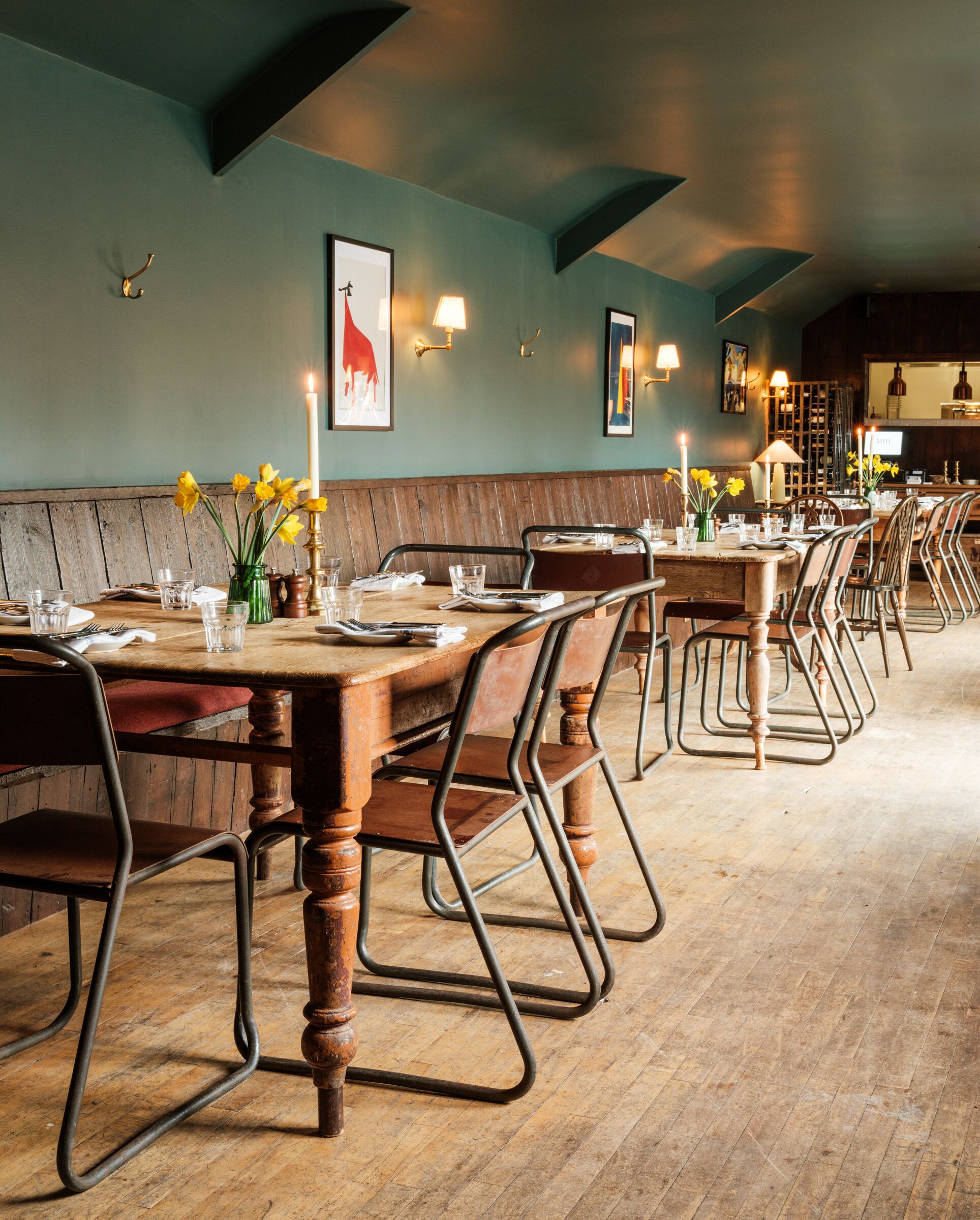 A restaurant with wooden tables and metal chairs, a wooden bench, and wall-mounted lights.