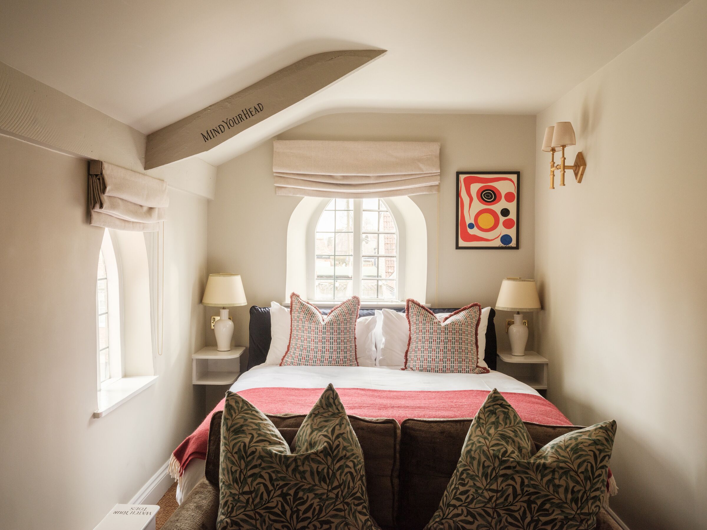 Een slaapkamer met een groot bed, twee nachtkastjes met lampen, een raam met gordijnen, en een kunstwerk aan de muur.