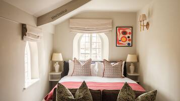 Een slaapkamer met een groot bed, twee nachtkastjes met lampen, een raam met gordijnen, en een kunstwerk aan de muur.