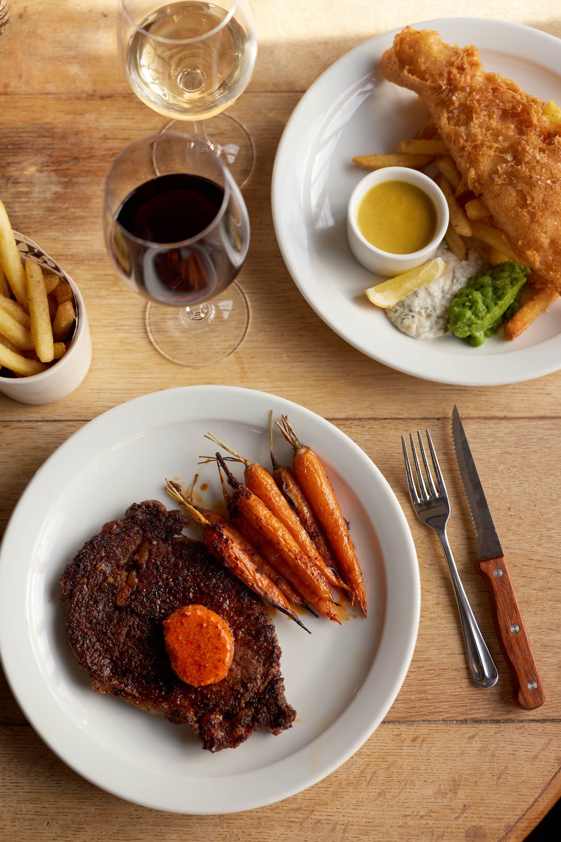 A wooden table with two plates of food, a glass of red wine, and cutlery.