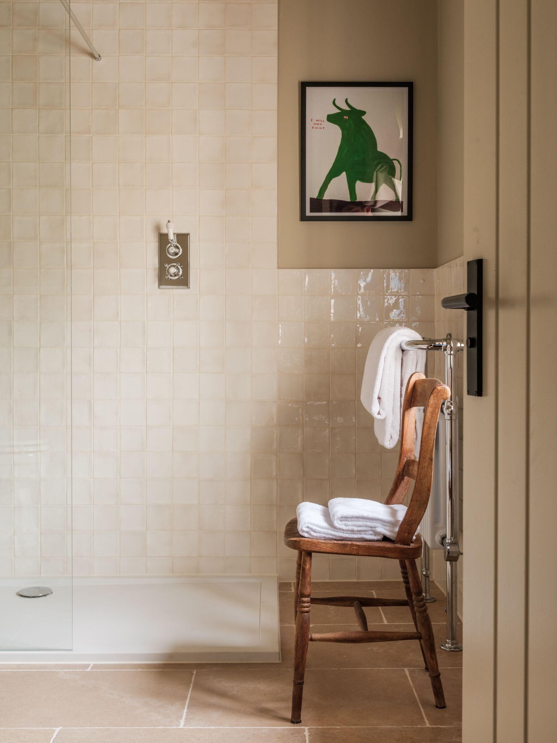 A bathroom with a shower, a wooden chair with towels, and a framed picture on the wall.