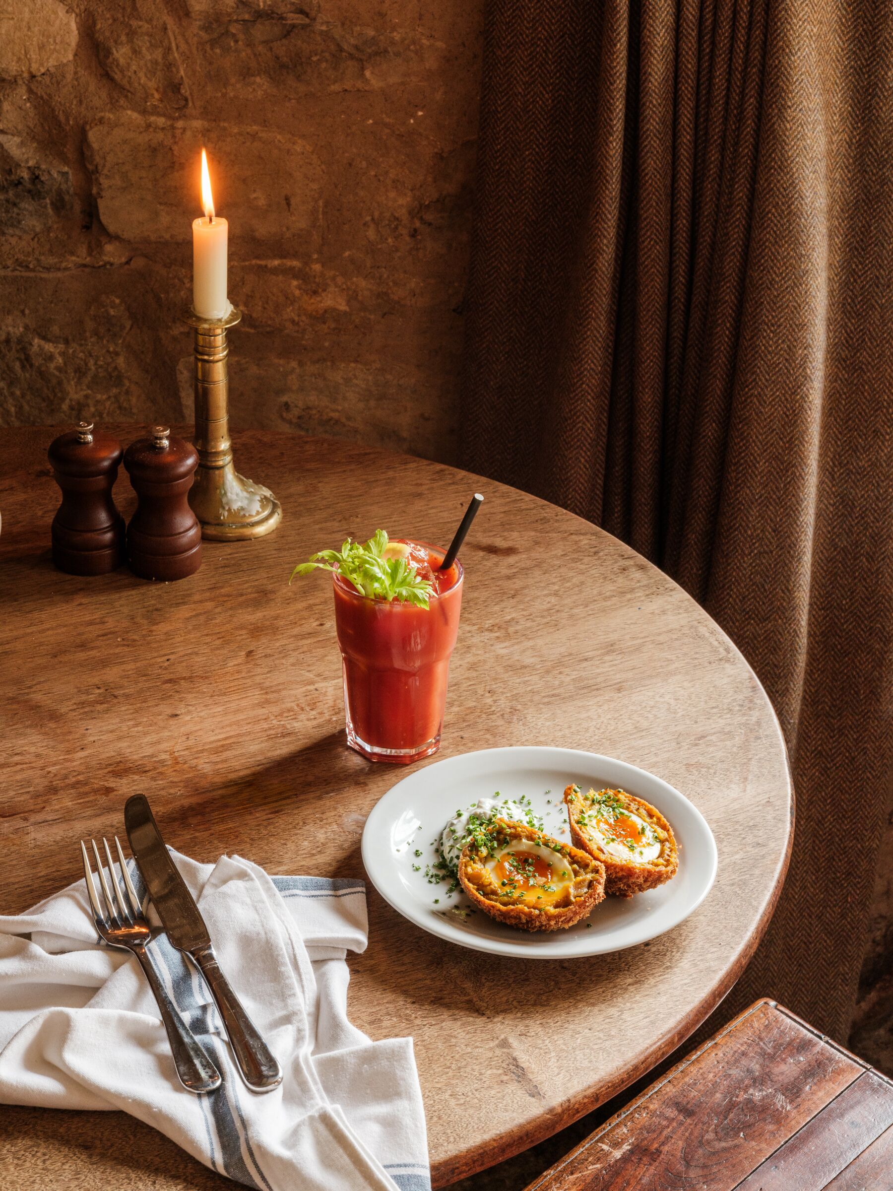 Un tavolo con una candela, un cocktail Bloody Mary e un piatto di cibo.