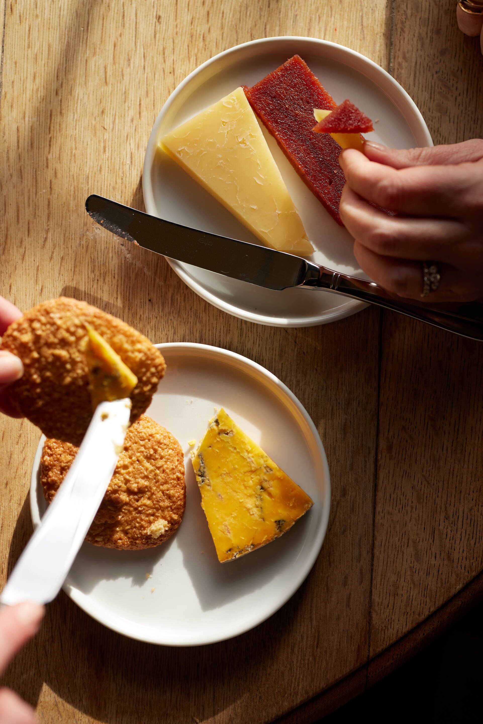 Ein Holztisch mit zwei weißen Tellern, einer mit einem Käse- und einem Fleischstück, der andere mit einem Keks und einer Käsescheibe.