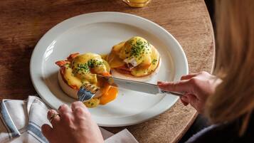 A dining table with a plate of eggs benedict and a glass of orange juice.