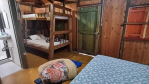 Ein Zimmer mit einem Etagenbett, einem Einzelbett, einer Holztür und einem kleinen Tisch mit Kissen.