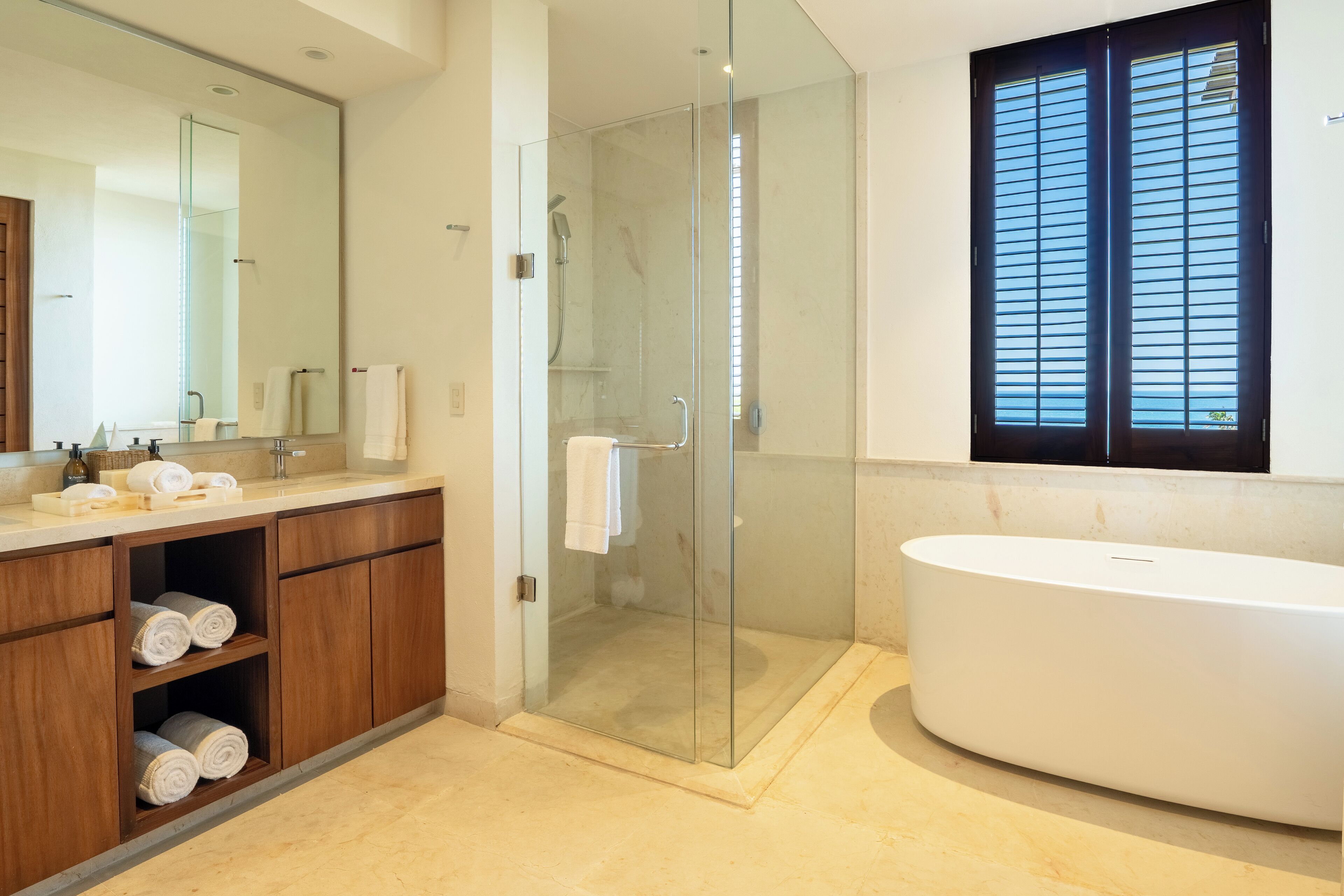 Une salle de bain moderne dotée d’une douche à parois de verre, d’une baignoire sur pieds et d’un meuble en bois où sont rangées les serviettes.
