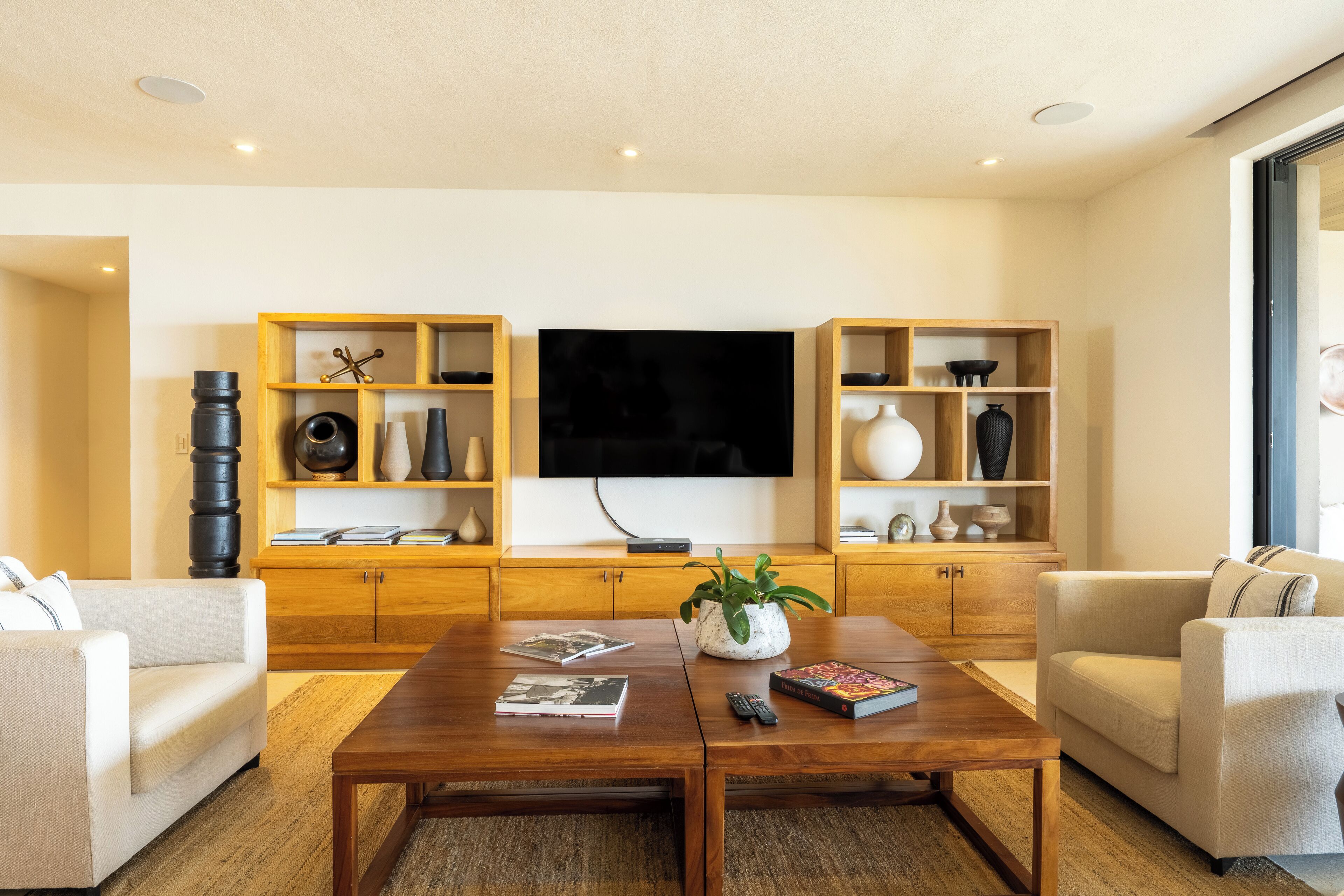 Een moderne woonkamer met een flatscreen televisie, houten kasten en een salontafel.
