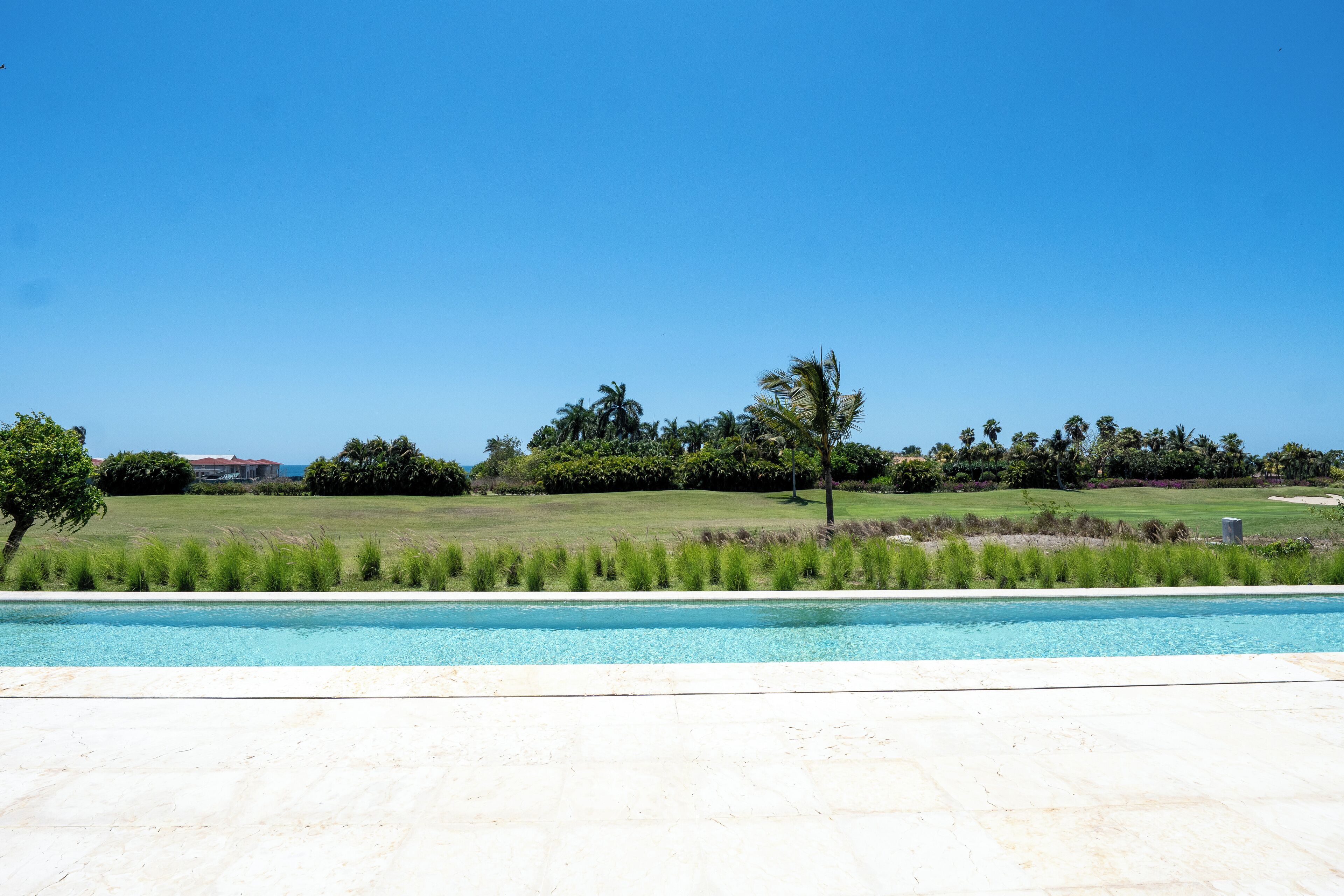 A swimming pool with a clear blue sky, a grassy area, and trees in the background.