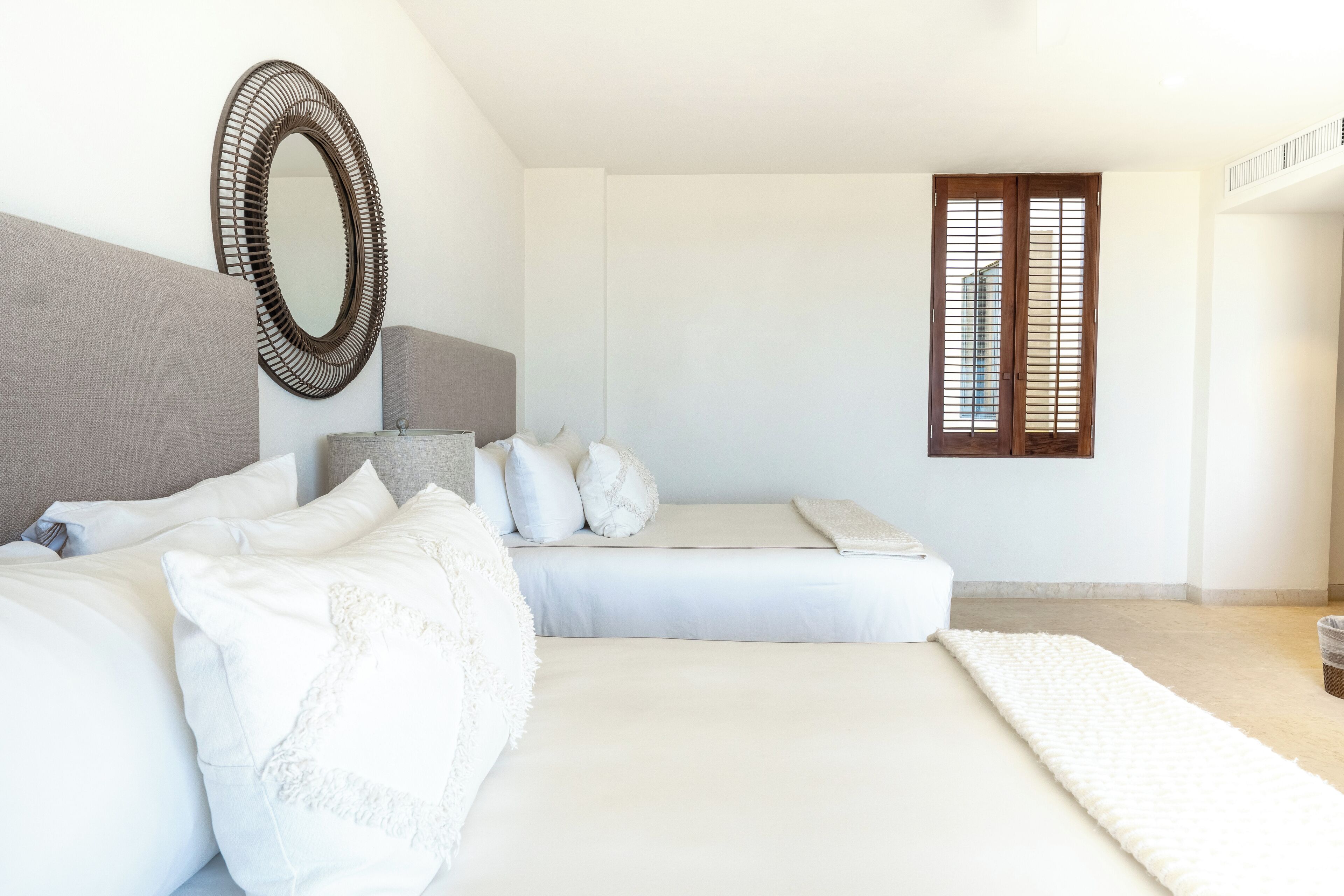 A bedroom with a large bed, a bedside table, a mirror, and a window with blinds.