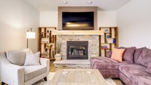 A living room with a stone fireplace, two sofas, a coffee table, and bookshelves. - Riverfront Retreat/Hot Tub/ Short Walk to Downtown (Bellaire)