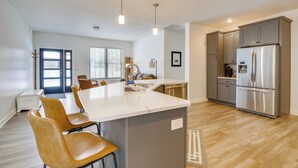 A modern kitchen with a central island, grey cabinets, stainless steel appliances, and a dining area with yellow chairs. - Riverfront Retreat/Hot Tub/ Short Walk to Downtown (Bellaire)