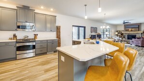 A modern kitchen with grey cabinets, a built-in oven, and a marble island with chairs. - Riverfront Retreat/Hot Tub/ Short Walk to Downtown (Bellaire)