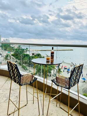 A balcony with two wicker chairs and a small table, overlooking a beach with palm trees and a pier. - Palmetto Eliptic  (Cartagena)