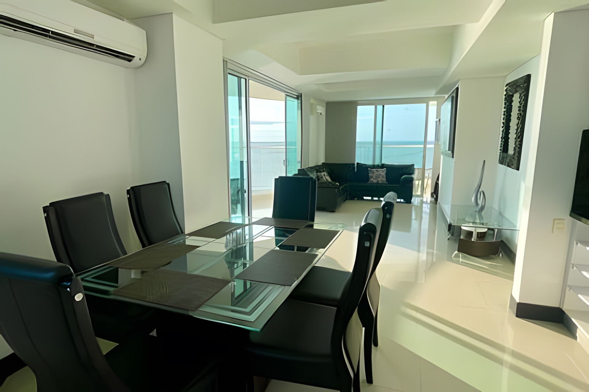 A modern living room with a glass dining table, black chairs, a sofa, and a TV.