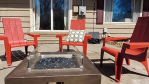 A patio with a glass-top fire pit, red chairs, and a table. - Charming 3-bedroom house, convenient location Overland Park (Overland Park)