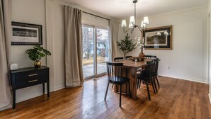 A dining area with a wooden table and chairs, a black side table with a plant, and a framed picture on the wall. - Charming 3-bedroom house, convenient location Overland Park (Overland Park)