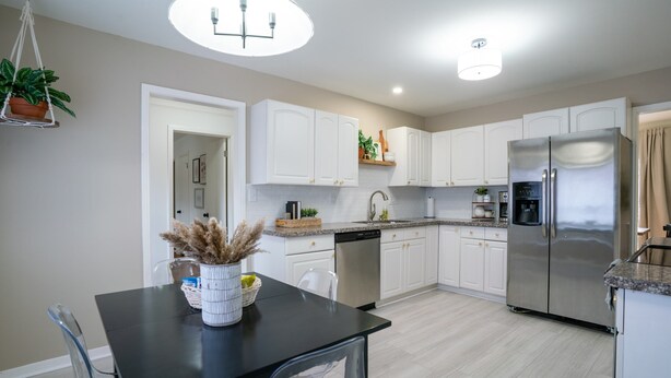 A modern kitchen with white cabinets, a stainless steel refrigerator, and a black dining table with chairs. - Charming 3-bedroom house, convenient location Overland Park (Overland Park)