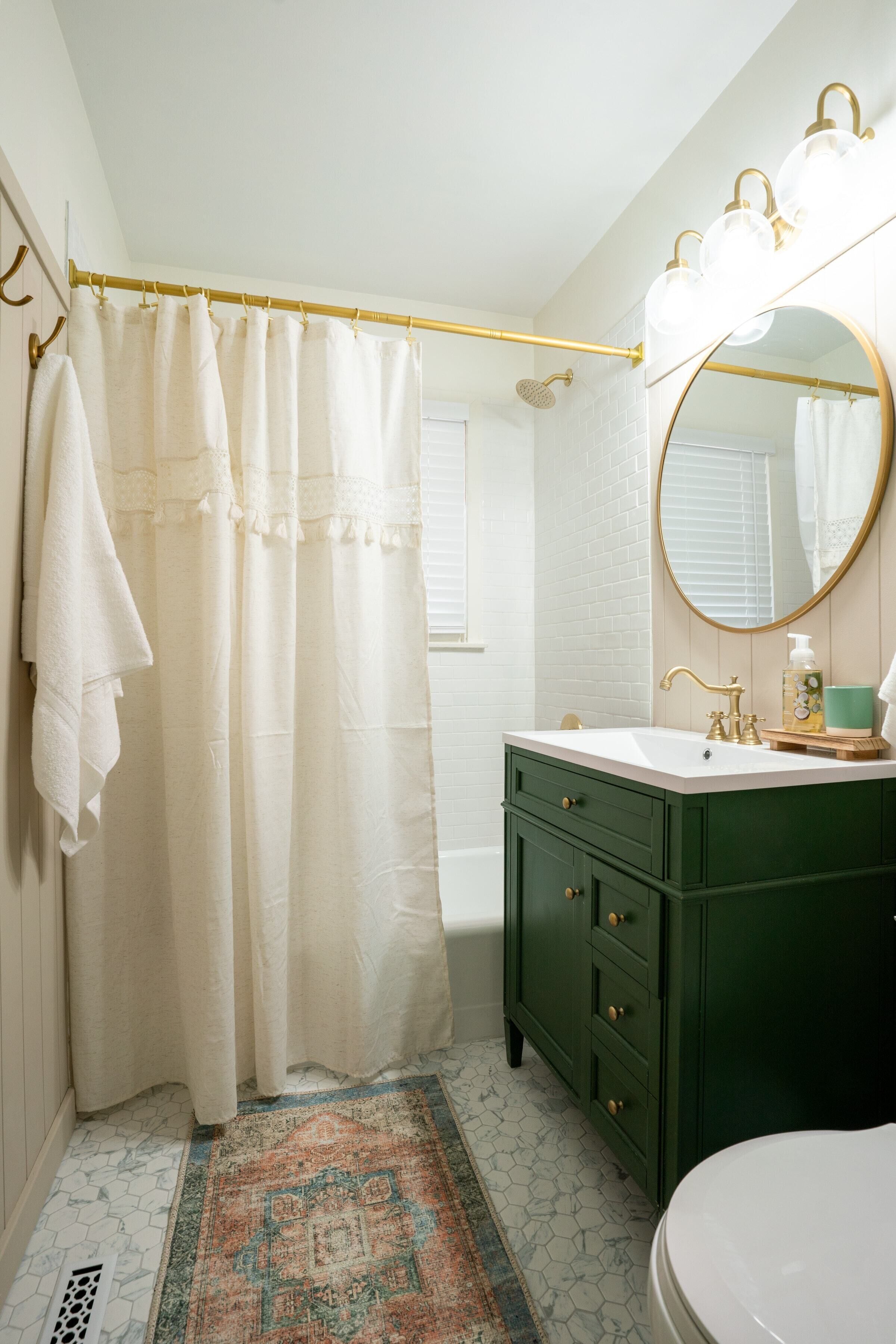 A bathroom with a white shower curtain, a green vanity with a round mirror, and a white toilet.